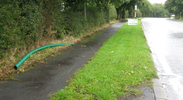 a long length of green pipe lying in the grass at the side of a wet road